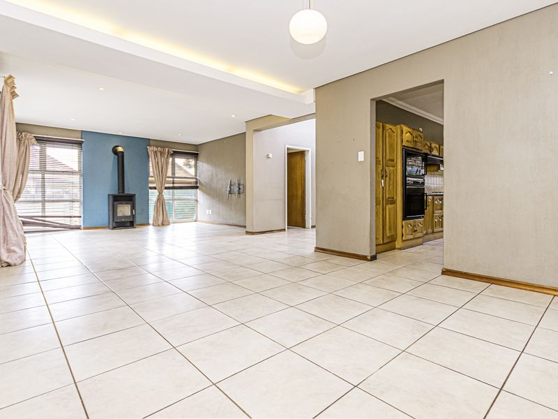 Spacious open-plan living area featuring tiled floors, a modern freestanding fireplace, and an exposed brick accent wall, with an adjacent kitchen visible.