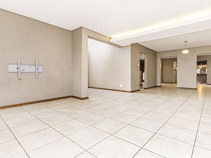Spacious, open-plan living area featuring neutral tiled flooring, recessed ceiling lighting, and a wall-mounted television bracket in a clean, vacant setting.