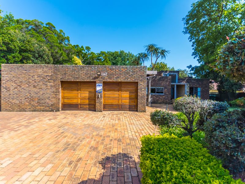 Front elevation of a brick house featuring a double garage, paved driveway, and established garden.