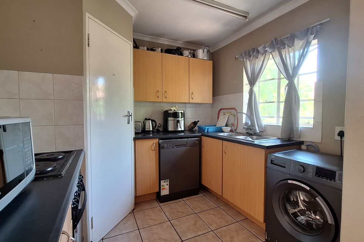 A functional kitchen featuring laminate cabinetry, tiled flooring, and integrated appliances, offering a practical layout with potential for modern cosmetic updates.