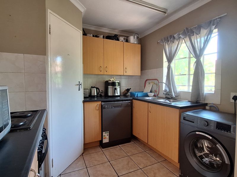 A functional kitchen featuring laminate cabinetry, tiled flooring, and integrated appliances, offering a practical layout with potential for modern cosmetic updates.