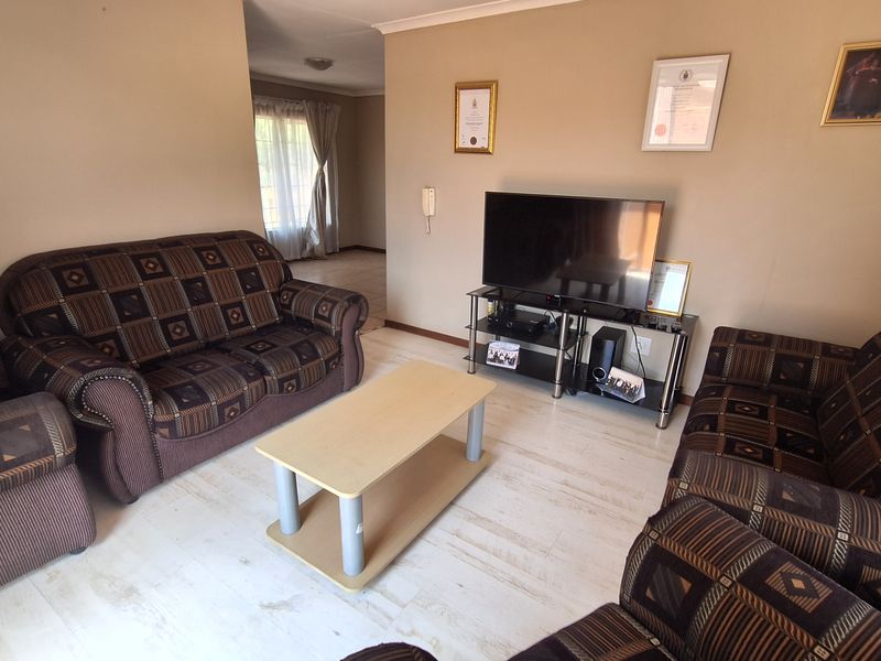 A living room featuring light-toned laminate flooring, neutral wall paint, and an intercom system, providing a functional and well-lit space.