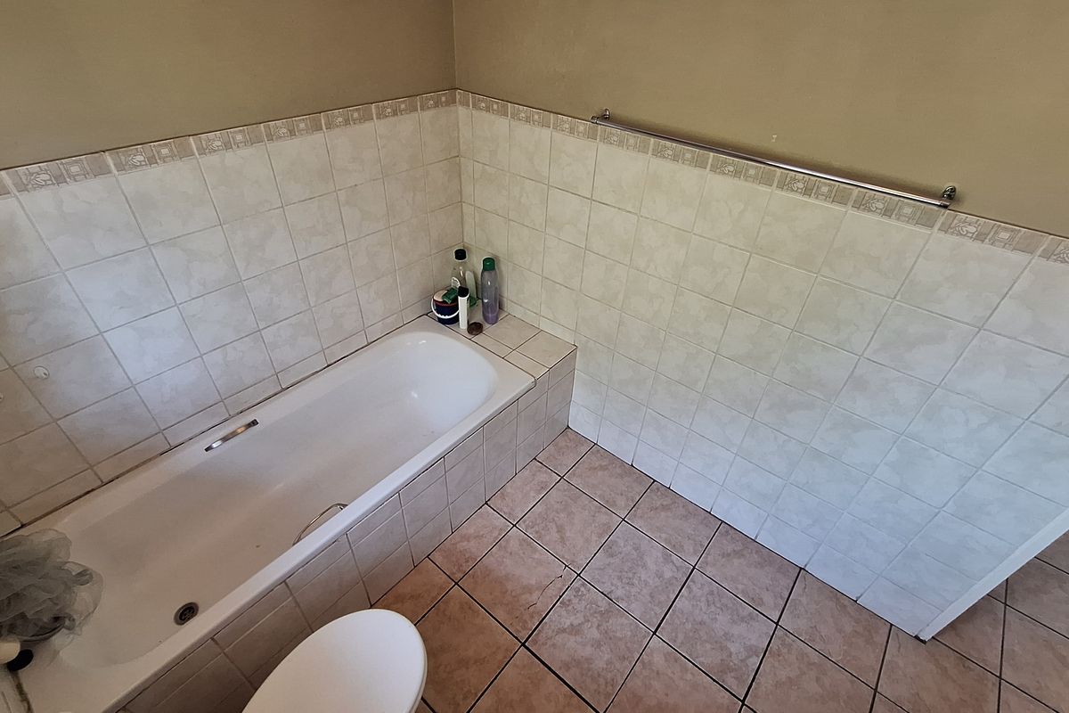 A functional bathroom featuring a built-in bathtub, tiled walls with a decorative border, and ceramic floor tiles.