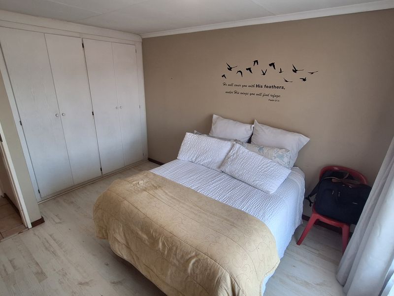 A bedroom featuring light-toned laminate flooring and built-in cupboards, with an adjacent view into a tiled bathroom area.