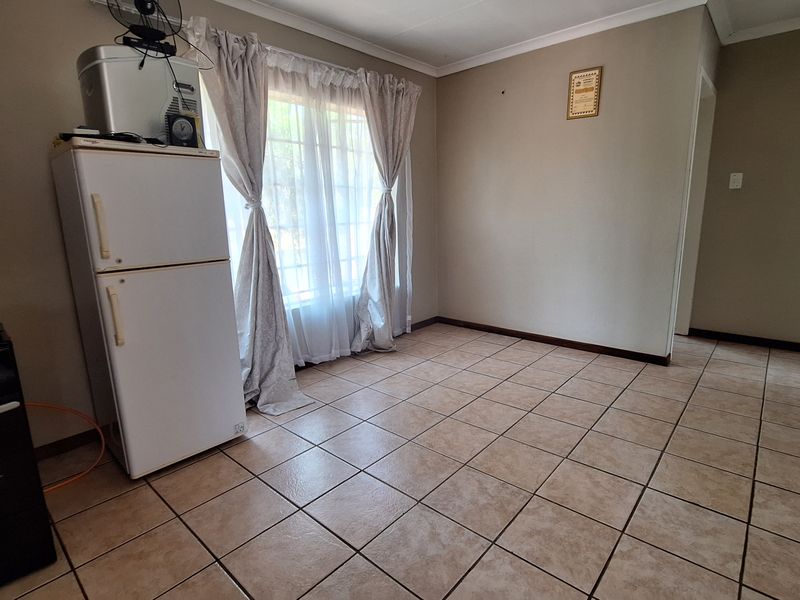 A spacious, neutrally painted living area featuring durable tiled flooring and natural light from a large window.