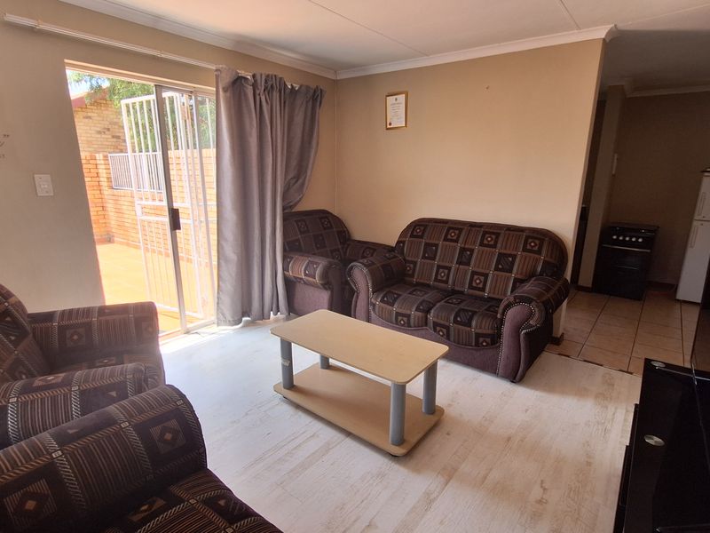 A functional living room featuring light-toned tiled flooring and a sliding glass door providing direct access to the outdoor patio area.