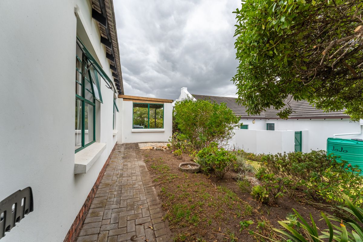 A side garden path featuring paved walkways, green-framed windows, and a water storage tank, leading towards the rear of the property.