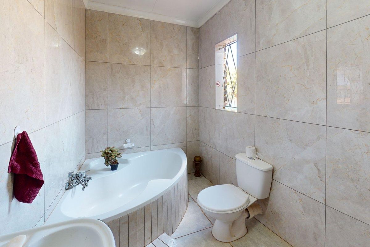 A clean, modern bathroom featuring full-height wall tiling, a corner bathtub, and a standard toilet.