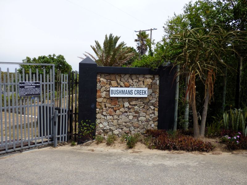 The entrance to Bushmans Creek featuring a stone masonry pillar, metal security gate, and established landscaping.