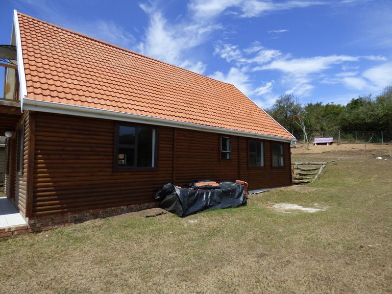 Rear view of a timber log cabin featuring a terracotta tiled roof, brick foundation, and surrounding garden area.