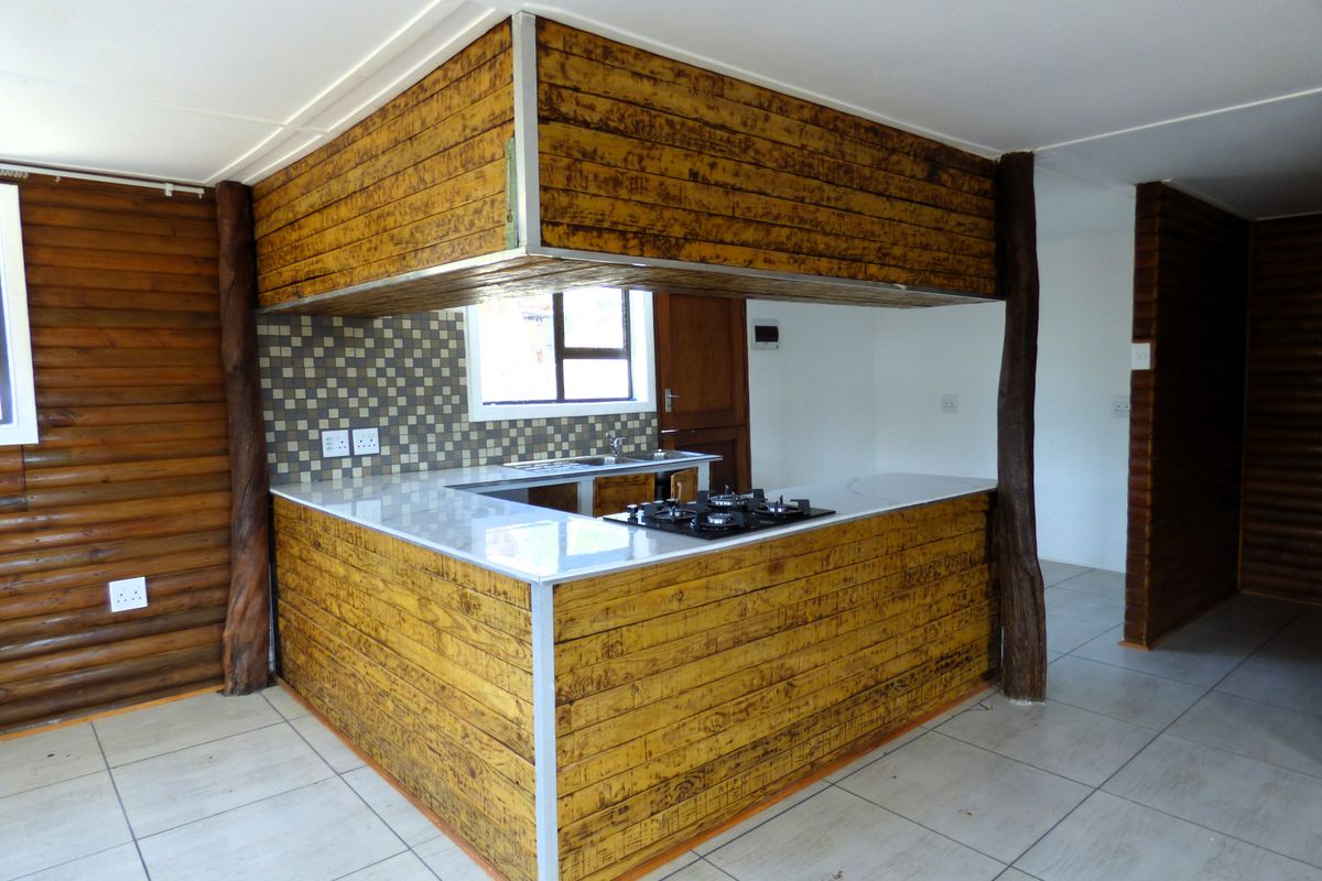 A rustic-style kitchen featuring timber-clad cabinetry, a stone countertop with an integrated gas hob, and neutral ceramic floor tiles.
