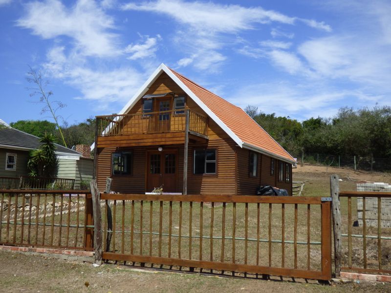 A charming timber log cabin featuring a pitched terracotta roof, a front balcony with wooden balustrade, and a secure wooden perimeter fence.
