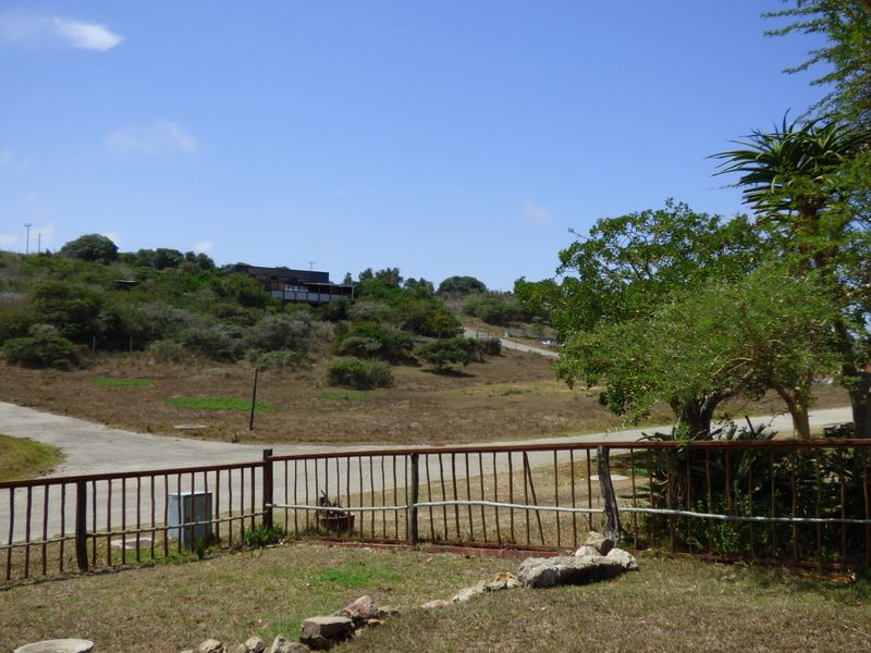 A wide-angle view of the surrounding landscape, featuring a paved road, natural vegetation, and a metal perimeter fence in the foreground.
