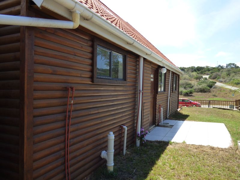 Rear view of a log cabin style house featuring timber siding, a tiled roof, and a small paved patio area.