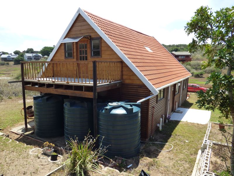 Rear view of a timber-clad house featuring a raised balcony, terracotta tiled roof, and multiple water storage tanks installed on the property.