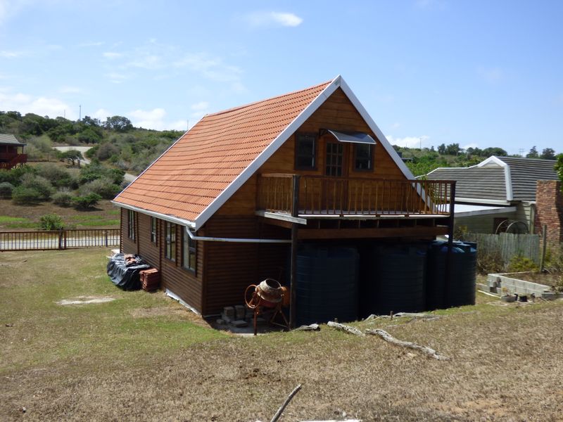 A rear view of a timber-clad house featuring a raised wooden balcony, tiled roof, and external water storage tanks set in a rural landscape.