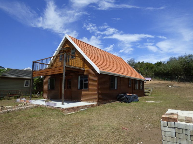 A detached timber log cabin featuring a terracotta tiled roof, a raised wooden balcony, and a concrete patio area set within a grassy plot.