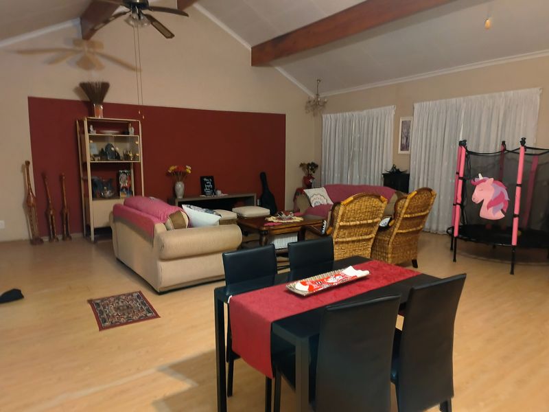Spacious open-plan living and dining area featuring vaulted ceilings with exposed timber beams, ceiling fans, and light-toned laminate flooring.