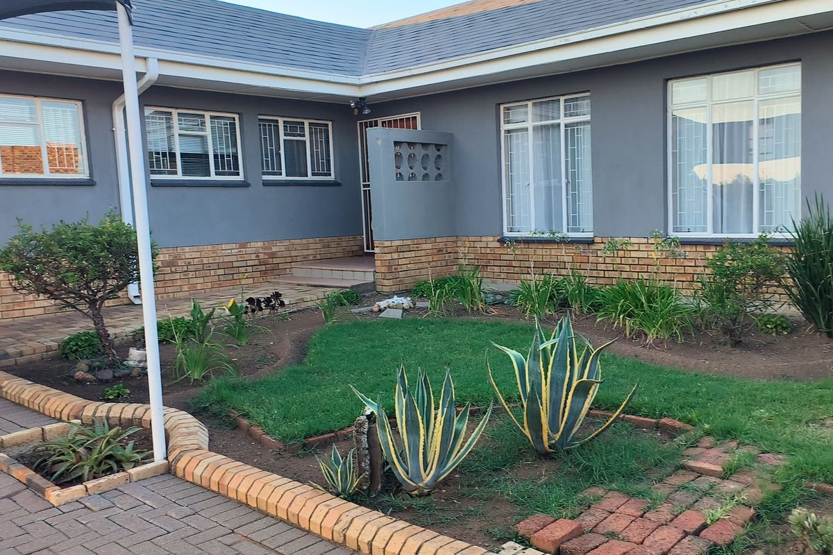 A rear exterior view of the house featuring a brick and painted facade, security-barred windows, and a landscaped garden with paved pathways.