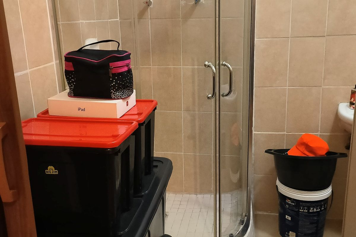 A bathroom featuring a corner shower enclosure with tiled walls and a pedestal basin, currently requiring maintenance to the shower fixtures.