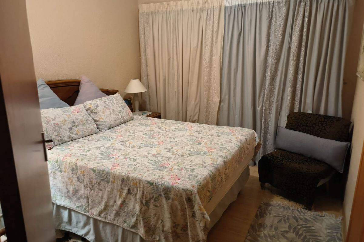 A functional bedroom featuring laminate flooring and full-length window curtains.