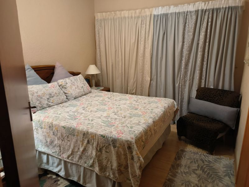 A functional bedroom featuring laminate flooring and full-length window curtains.