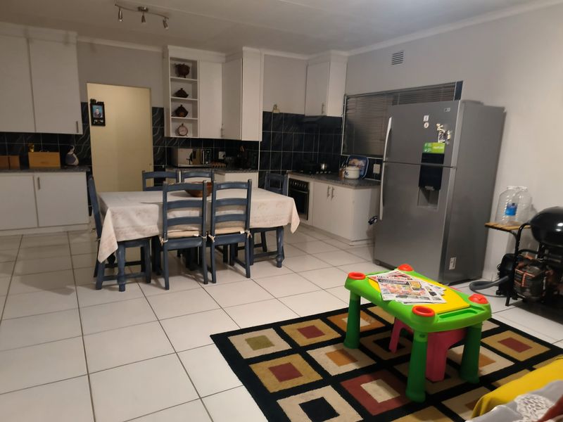 Open-plan kitchen and dining area featuring white cabinetry, tiled flooring, and a dark tiled backsplash, offering a functional layout for family living.