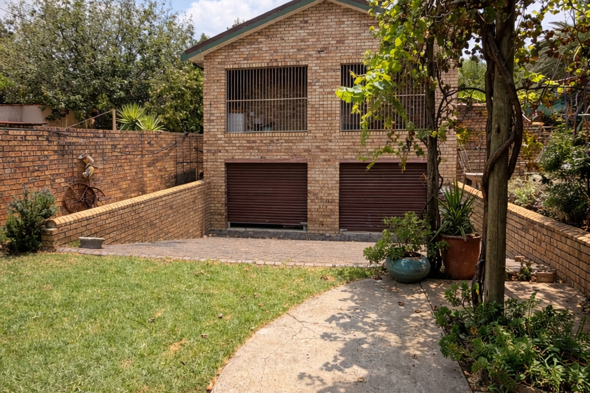 Rear view of a face brick double garage featuring roller shutter doors, security bars, a paved driveway, and a garden area with a pergola.