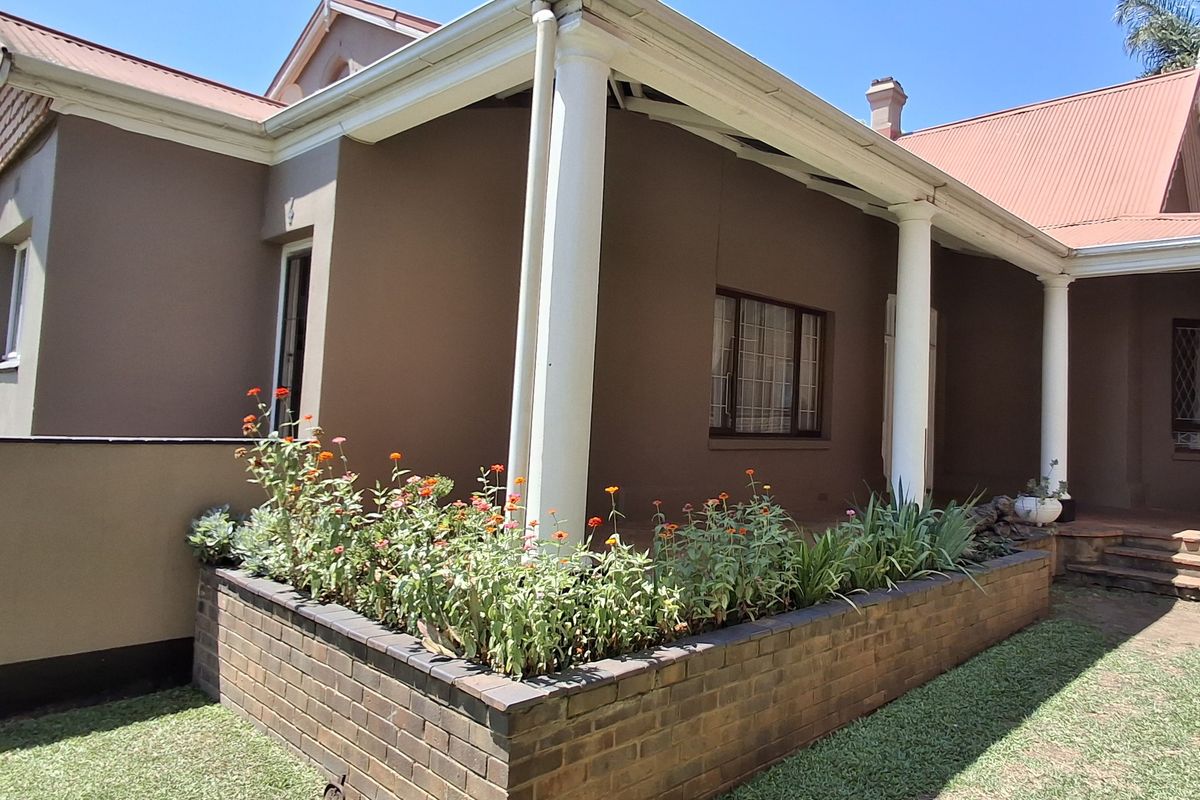 A view of the rear exterior featuring a covered patio area with structural columns and a brick planter box in the garden.