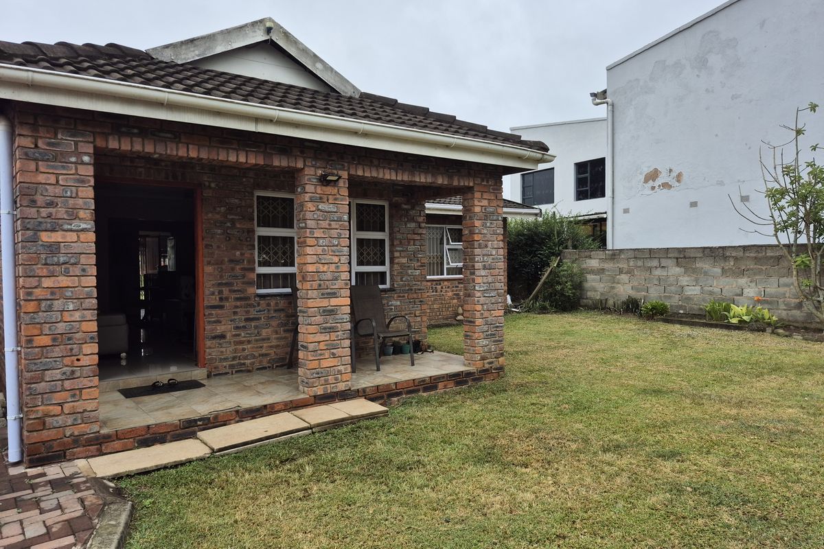 Rear view of a face brick house featuring a covered patio, tiled roof, and a private garden area with a concrete block boundary wall.
