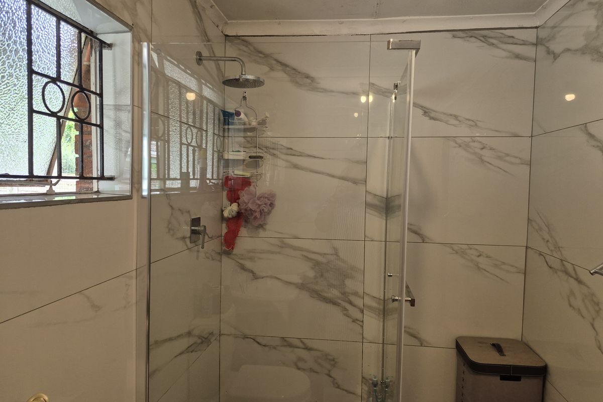 Modernized bathroom featuring a walk-in shower with marble-look wall tiles, a rain shower head, and a glass screen.