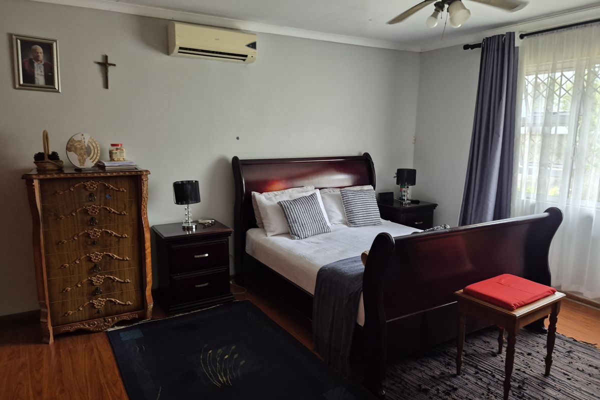 A well-maintained bedroom featuring laminate flooring, a ceiling fan, and a wall-mounted air conditioning unit.
