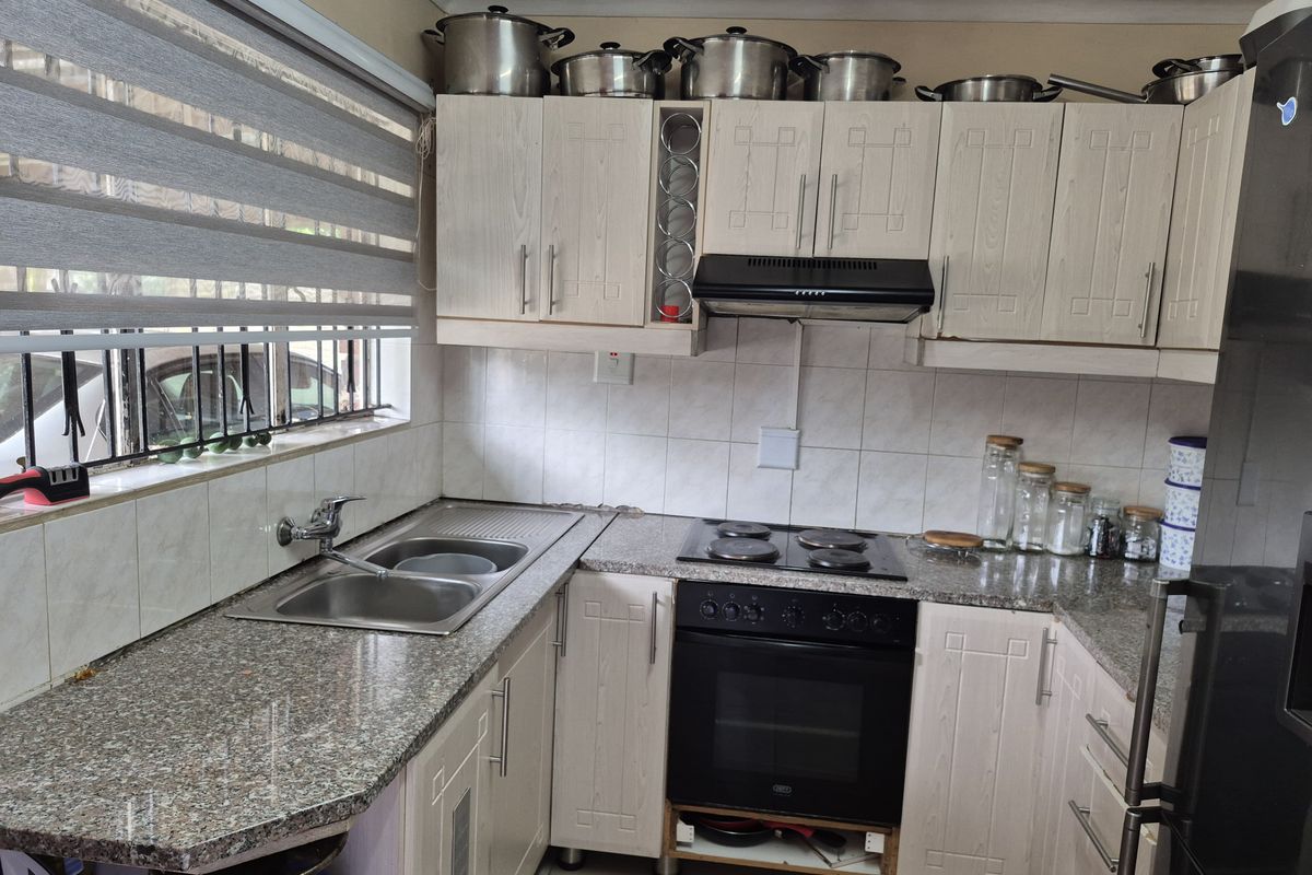 Functional kitchen featuring granite countertops, built-in oven with hob, extractor fan, and ample cabinetry with a tiled backsplash and roller blinds.