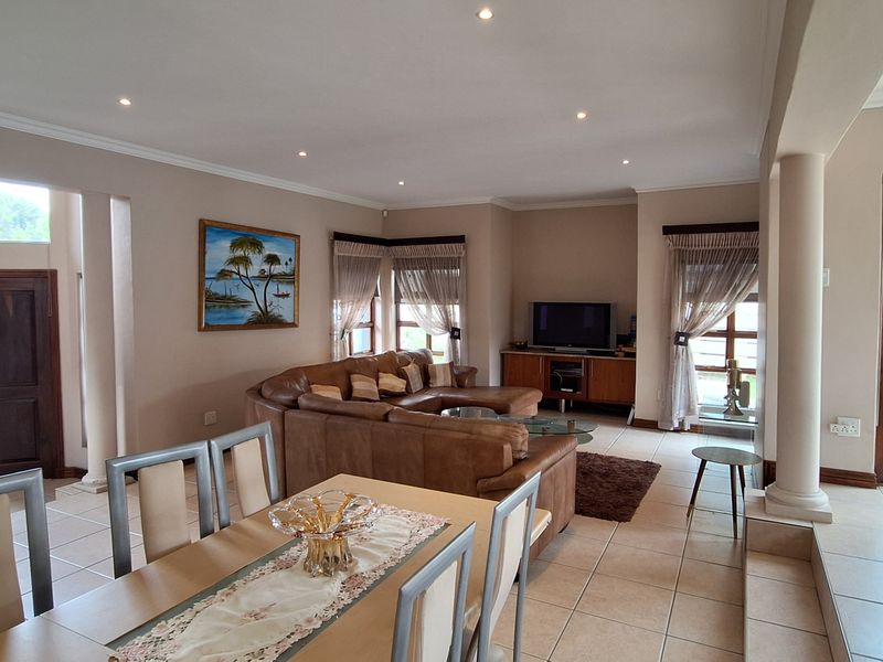 Spacious open-plan living and dining area featuring neutral wall tones, tiled flooring, recessed lighting, and architectural columns connecting the interior spaces.