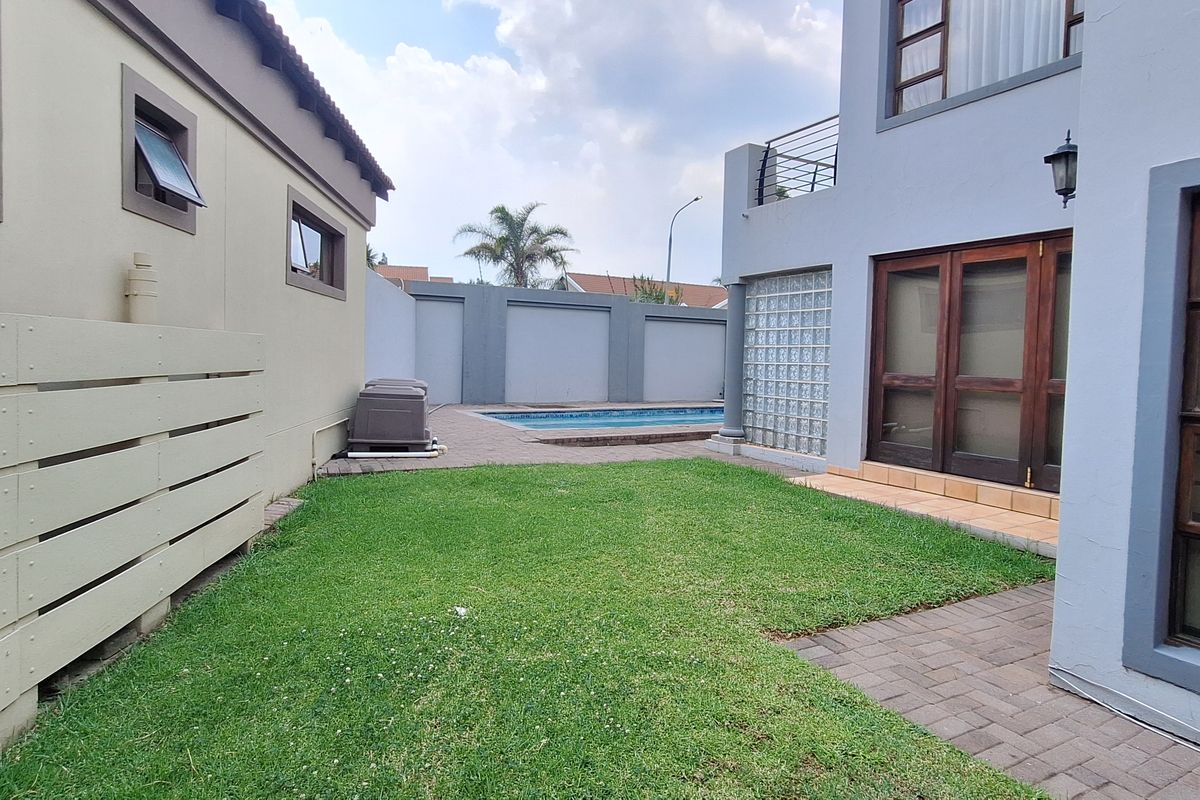 Rear garden area featuring a swimming pool, paved patio, lawn, and access to the main dwelling via timber-framed doors and glass block features.
