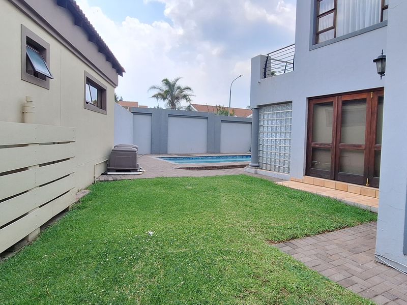 Rear garden area featuring a swimming pool, paved patio, lawn, and access to the main dwelling via timber-framed doors and glass block features.