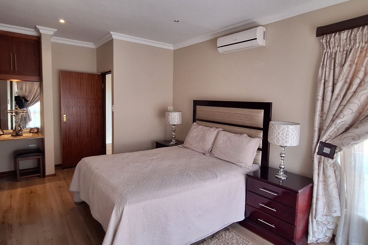 A well-maintained bedroom featuring laminate flooring, a built-in vanity area, and a wall-mounted air conditioning unit.