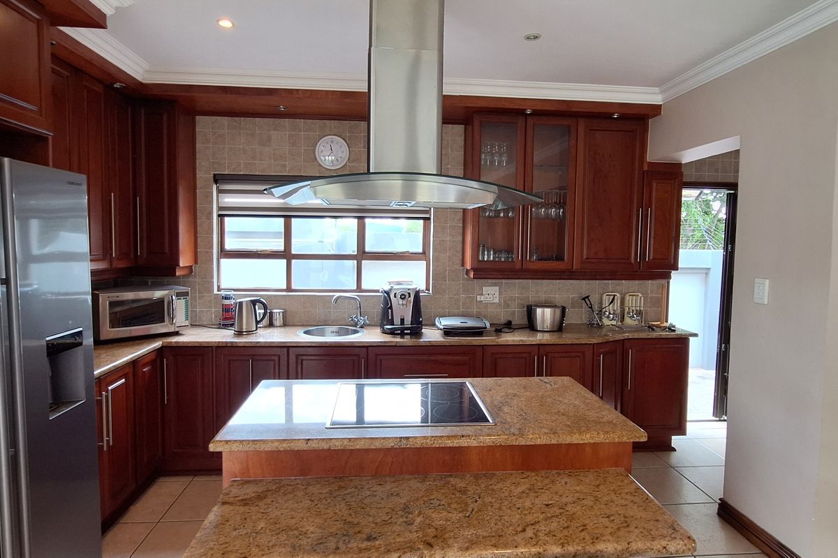 A well-maintained kitchen featuring rich wooden cabinetry, granite countertops, a central island with a built-in hob, and a stainless steel extractor fan.