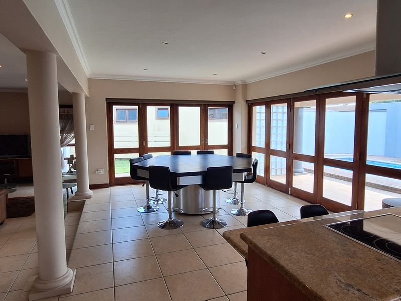 Spacious open-plan living and dining area featuring tiled floors, granite kitchen countertops, and large wooden folding doors opening to the outdoor pool area.