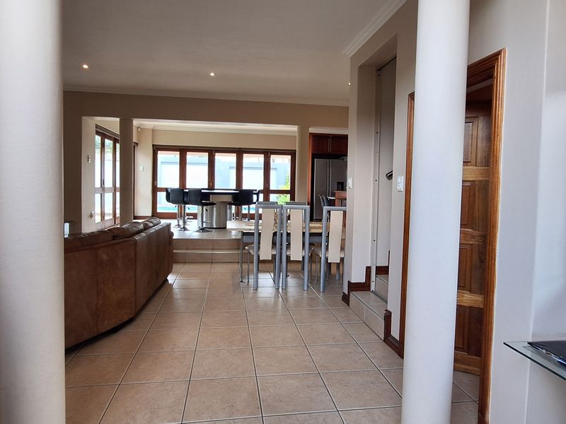 Spacious open-plan living and dining area featuring tiled flooring, structural columns, and bi-fold doors leading to an outdoor space.