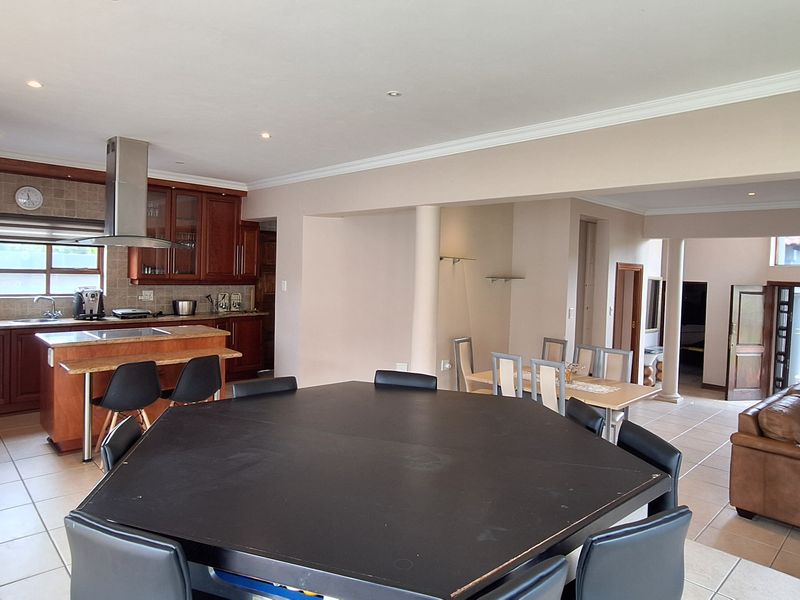 Spacious open-plan living area featuring a kitchen with wooden cabinetry, a central island, and tiled flooring, flowing into the dining and lounge spaces.