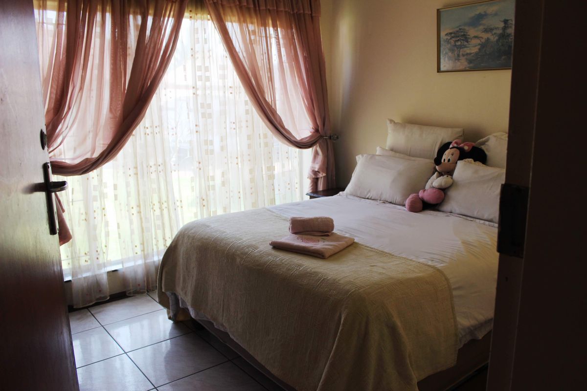 A bedroom featuring tiled flooring and a large window with curtains, providing natural light to the space.