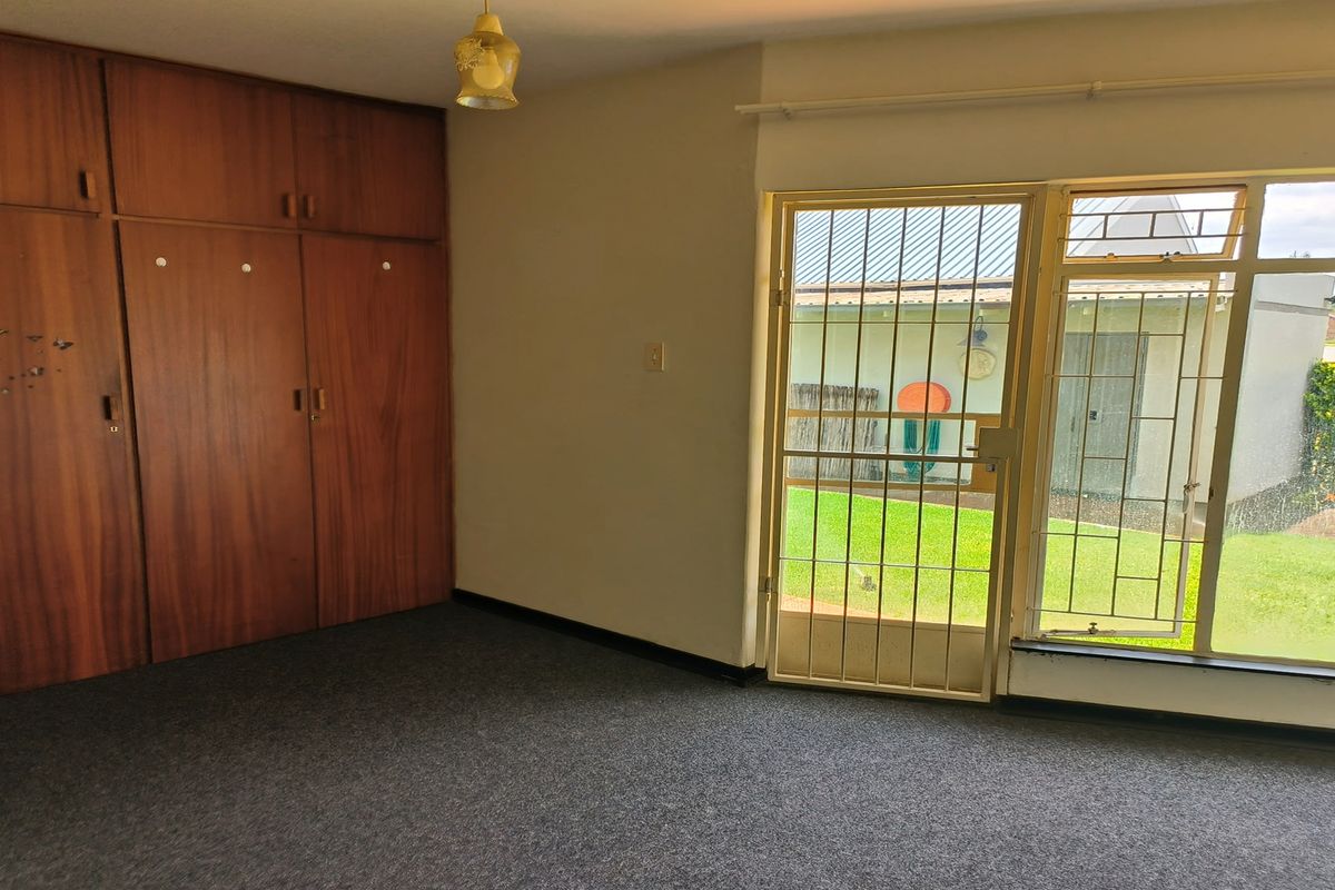 A bedroom featuring built-in wooden cupboards, carpeted flooring, and a security gate providing access to the garden area.