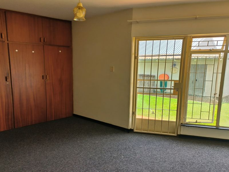 A bedroom featuring built-in wooden cupboards, carpeted flooring, and a security gate providing access to the garden area.