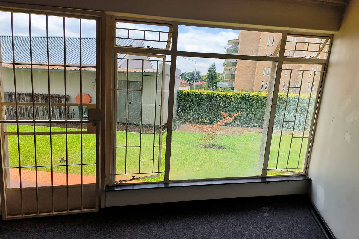 Interior view of a living area featuring large windows with security bars, overlooking a private garden space.