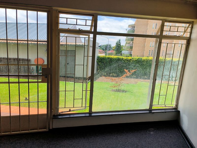 Interior view of a living area featuring large windows with security bars, overlooking a private garden space.