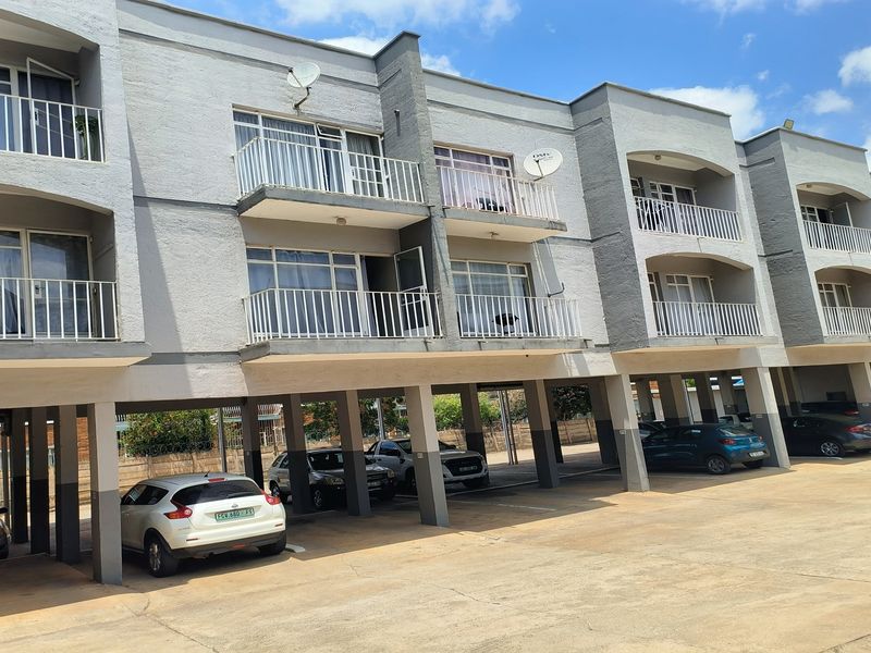 Exterior view of a multi-story townhouse complex featuring covered ground-level parking bays and private balconies for each unit.