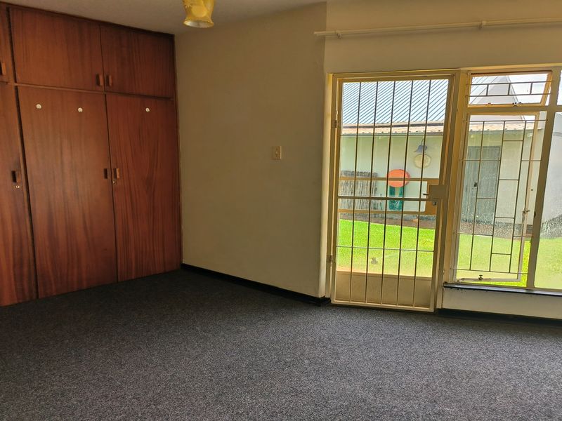 A bedroom featuring built-in wooden cupboards, grey carpeting, and a security gate leading to the exterior garden area.