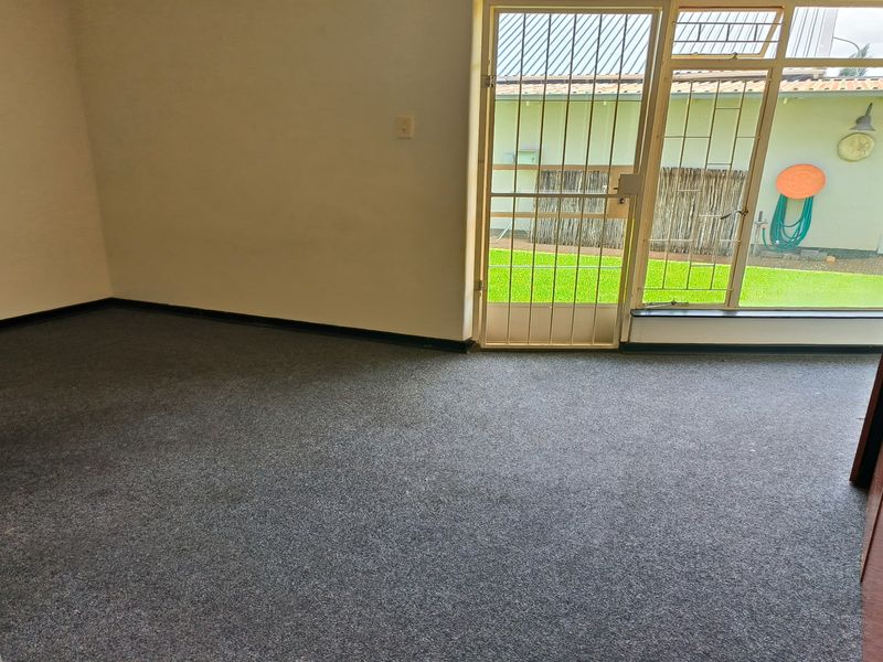 An empty living room featuring grey carpeting and a security gate leading to an outdoor garden area.