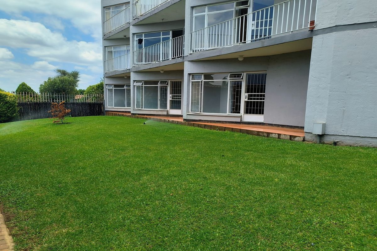 Rear view of a multi-story townhouse complex featuring a shared lawn, paved patio areas, and metal balcony railings.